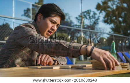 Man playing giant wooden dominoes, He is sitting at a wooden table 