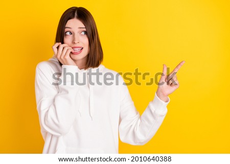 Photo of nervous lady biting finger direct empty space look side wear white hoodie isolated yellow color background