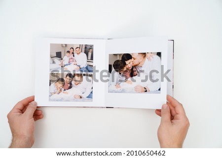 on a white background, hands flip through a photobook from a home family photo shoot with a newborn child. traditions to make a photo album and print photos from important moments of life. Royalty-Free Stock Photo #2010650462