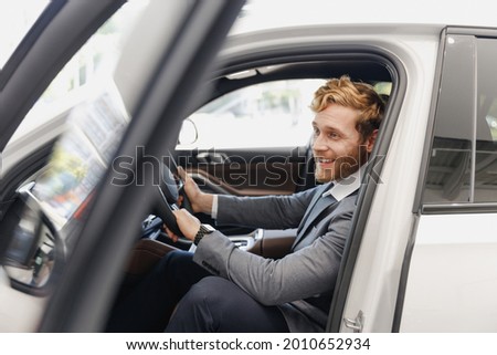 Side view fun man customer male buyer client wear classic grey suit driving car hold wheel choose auto want buy new automobile in showroom vehicle salon dealership store motor show indoor Sale concept