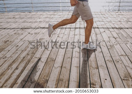 Cropped leg photo shot young strong sporty athletic fit sportsman man wearing sports clothes shorts warm up training jog run at sunrise sun over sea beach outdoor on pier seaside in summer day morning