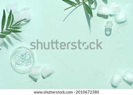 Self made moisturizer with ice cubes and exotic palm leaves on mint green background. Minimal flat lay, top view with copy-space, place for text or product. Facial massage concept, handmade cosmetics.