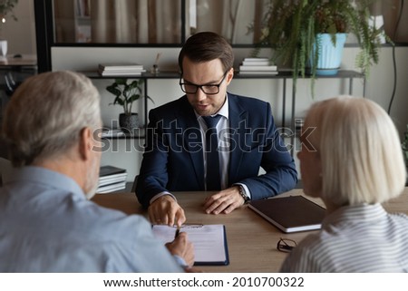 Confident lawyer, real estate agent, financial advisor giving consultation to mature couple of clients, explaining legal documents, helping to paper form, contract, agreement for signing. Royalty-Free Stock Photo #2010700322