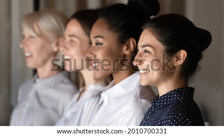 Side view row of diverse female staff of company, multiethnic female department, business leaders of different ages. Young Indian employee, professional, teacher standing with coworkers, smiling