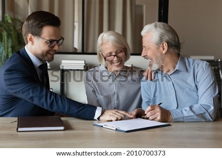 Happy senior couple signing medical insurance agreement, real estate lease contract in agent office. Elderly man and woman filling paper form, meeting with lawyer, solicitor, broker, realtor Royalty-Free Stock Photo #2010700373