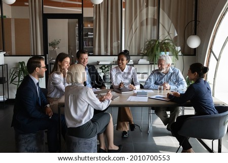 Multiethnic business team, employees of different ages discussing project strategy, brainstorming, talking and laughing in meeting room. Asian mentor, leader training group of interns, teaching staff. Royalty-Free Stock Photo #2010700553