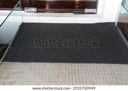 Black grey welcome door mat in front of door.