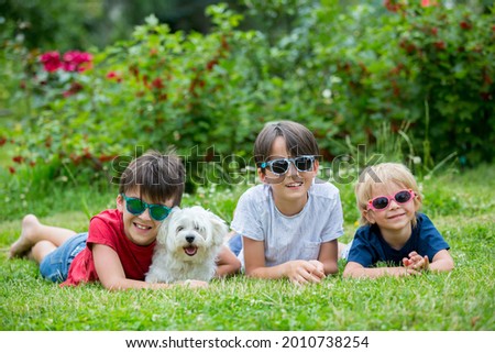 Three children and cute white puppy pet dog with sunglasses, having fun in garden, summertime