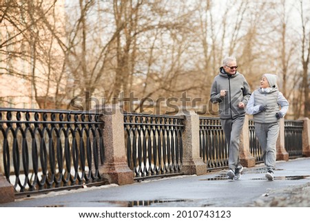 Full length wide angle view at active senior couple running outdoors in winter