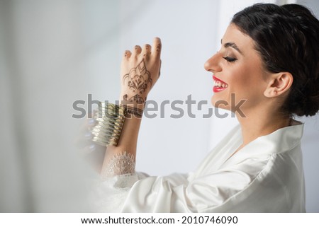 young and happy indian bride smiling and wearing golden bracelet on white