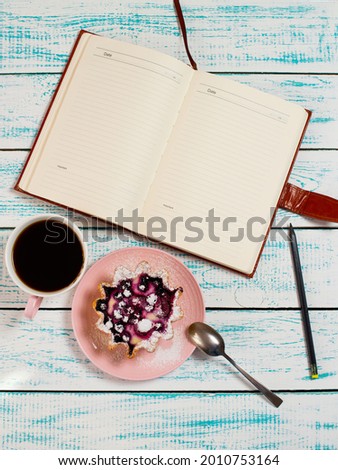Notepad, a cup of coffee and a cake basket with berries and cottage cheese on a vintage blue and white color. Morning breakfast background. Flatley coffee break layout.