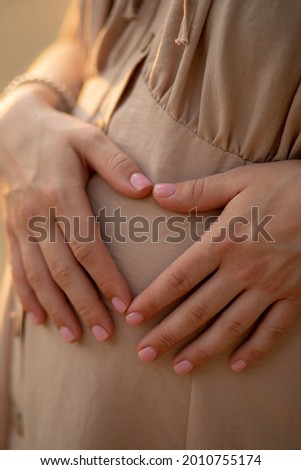 a pregnant woman in a beige dress holds a hand on a tummy. Waiting for a baby, pregnant photo session. pregnancy and childbirth in the summer, 9 months. motherhood concept