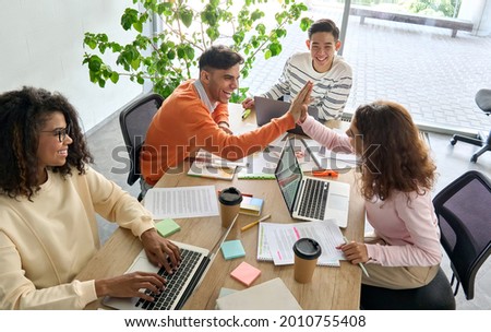 Young happy laughing creative team four multicultural coworkers or college students group celebrate success together giving highfive in office classroom. Top view. Great teamwork result high five Royalty-Free Stock Photo #2010755408