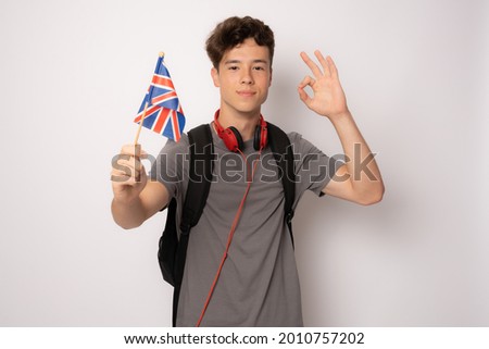 Cute student in casual clothes posing with british flag with okay sign isolated over white background.