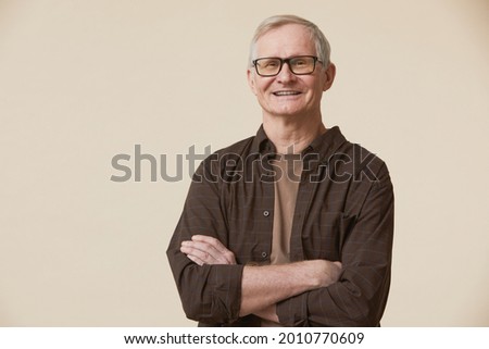 Minimal waist up portrait of senior man wearing glasses and looking at camera while standing with arms crossed against beige background Royalty-Free Stock Photo #2010770609