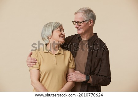 Minimal waist up portrait of carefree senior couple embracing and looking at each other while standing against beige background Royalty-Free Stock Photo #2010770624