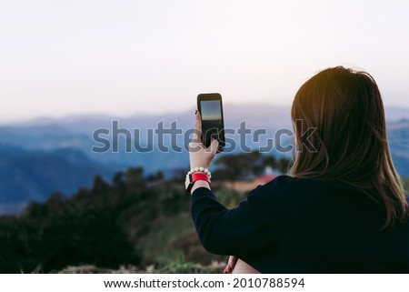Asian female tourists use their mobile phones to take pictures of the scenery at the top of a fresh mountain hill.