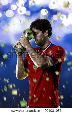 Chilean soccer player, celebrating the championship with a trophy in his hand. On a blue lights background.