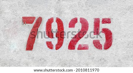 Red Number 7925 on the white wall. Spray paint. Number seven thousand nine hundred and twenty five.