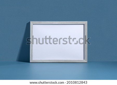 Blank picture frame leaning against blue wall. Invitation mockup, long shadow.
