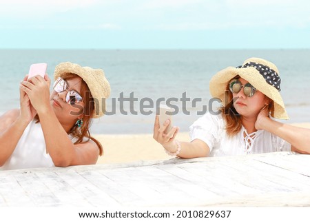 Portrait of young twins asian women at beautiful beach. Travel on vacation in summer season. Girls use cellphone to selfie, enjoy on holidays in tropical island.