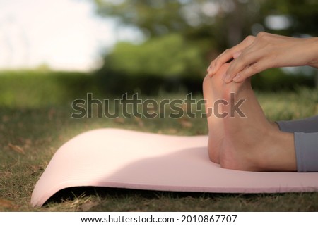 Close up of woman hands reach to toe to stretching her body on yoga mat at garden. Relaxing, practicing, streching, warm up, cool down after or before workout.