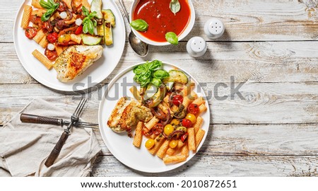 Food banner. Grilled turkey fillet, penne pasta with tomatoes, spices, Parmesan cheese and fresh basil. Tomato sauce. Traditional Italian cuisine. Two servings on a wooden background. Copy space Royalty-Free Stock Photo #2010872651