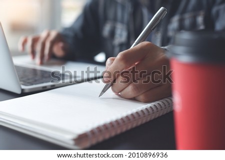 E-learning, online study, on line working from home concept. Business woman with a pen in hand writing on paper notebook and searching the internet on laptop computer. student studying online class