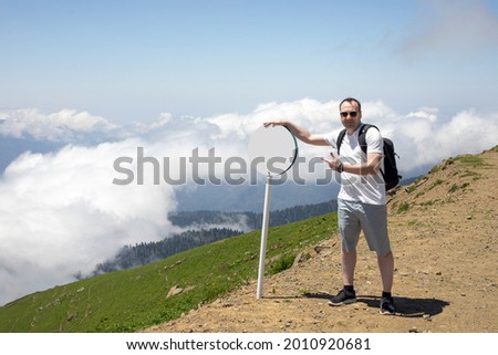 young man - tourist on the top of the mountain, points to a road sign