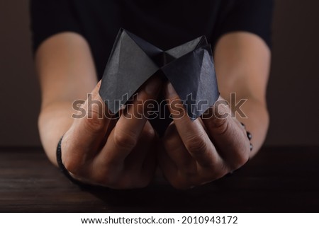 Hands of male fortune teller with paper cootie catcher on dark background