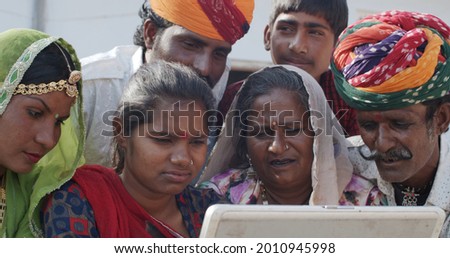 A group of South Asian people in traditional Indian clothing using a laptop together