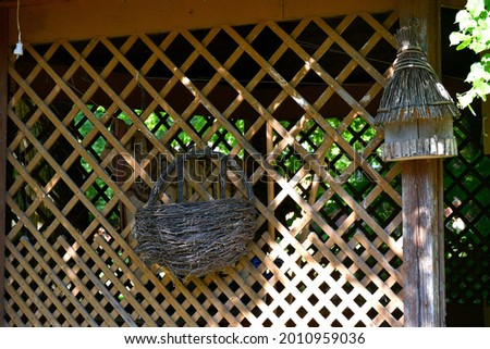 A close up on a straw or wicker basked attached to a wooden fence or wall with a small bird feeding shack located nearby spotted in the middle of a rural Polish village on a sunny summer day
