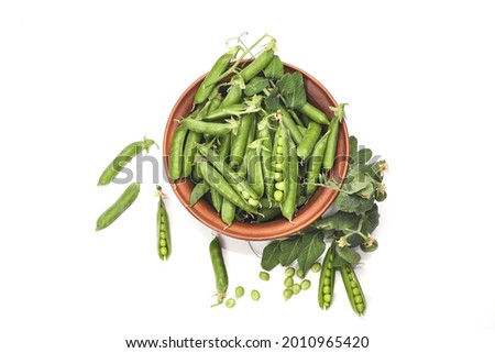 Pods of green peas with leaves in bowl isolated on white background