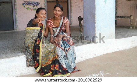 Two South Asian women wearing traditional costumes and looking at something while talking