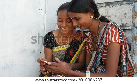 The two young Indian females in traditional clothes having fun together and using a smartphone