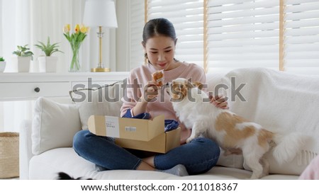Young happy asia people girl smile enjoy with cute dog unbox snack food post mail sit relax at home comfort sofa couch in omni channel fast send parcel via online sale pet shop store e-commerce order. Royalty-Free Stock Photo #2011018367
