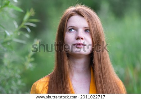 Portrait of a beautiful red-haired girl in the green grass in summer.