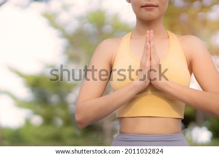 Crop woman in yellow sport bra pressed hands at chest doing  meditation poseture with green bokeh background.
