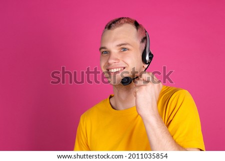 European handsome young man in yellow t shirt on pink background with headphones, young call centre worker manager happy cheerful smiling
