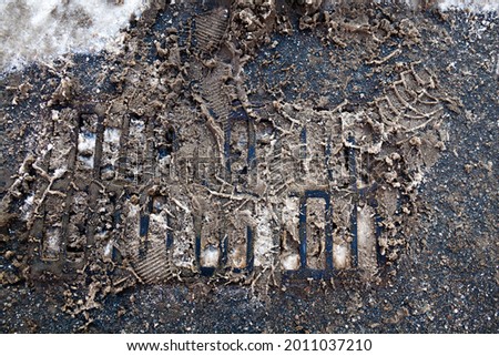 Drain grate with dirty snow on the road in winter. Wheel tracks on the snow.