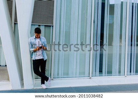 Handsome young caucasian man using phone at the city with wireless headphones.