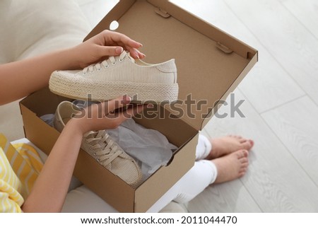Woman with canvas shoes and box on sofa, closeup Royalty-Free Stock Photo #2011044470