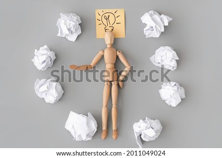 Wooden mannequin, drawn light bulb and crumpled paper balls on grey background