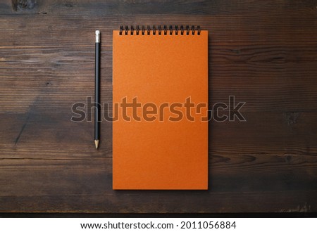 Blank orange notebook and pencil on wooden background. Stationery mock up. Flat lay.