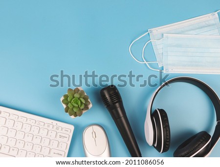 Top view or flat lay of computer keyboard, mouse, microphone, headphones and medcal face masks on blue background. Online teaching or online meeting during Covid19 lockdown.