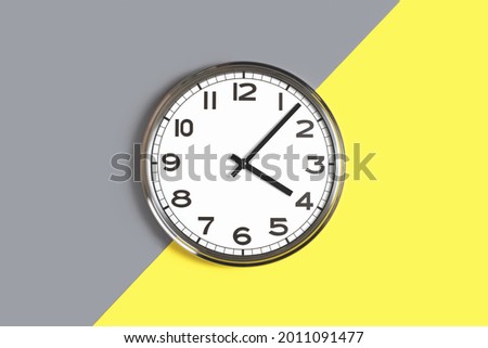 Plain wall clock in the center of grey and yellow background. Four o'clock. Close up banner with copy space, time management or school concept and lunch time. Opening or closing hours. Schedule