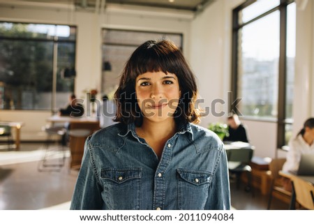 Portrait of female executive in office with colleagues working in background. Young businesswoman in co-working space.