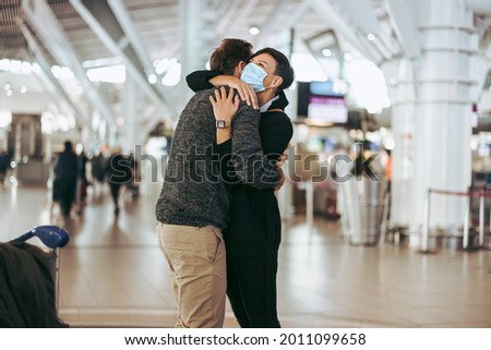 Woman in face mask giving welcome hug to man at airport arrival gate. Woman wearing face mask welcoming and embracing her boyfriend at airport Royalty-Free Stock Photo #2011099658