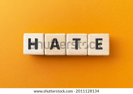 Text HATE on wooden cubes on bright orange ocher background. 
Feel intense or passionate dislike. Square wood blocks. Top view, flat lay.