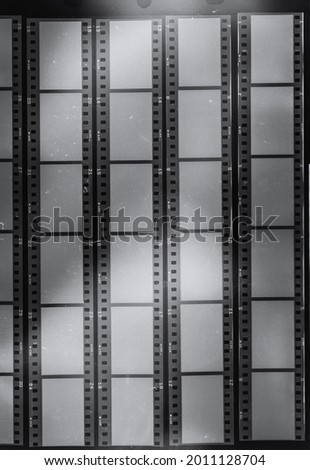 long empty 35mm film strips behind protection foil on black background, black and white film material with blank windows.